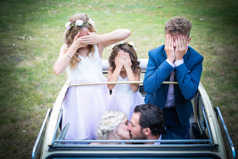Mariage photos de couple des mariés qui s'embrassent dans une 2 CV avec les enfants à coté Emilie Champeyroux Photographies Auvergne Riom Aigueperse